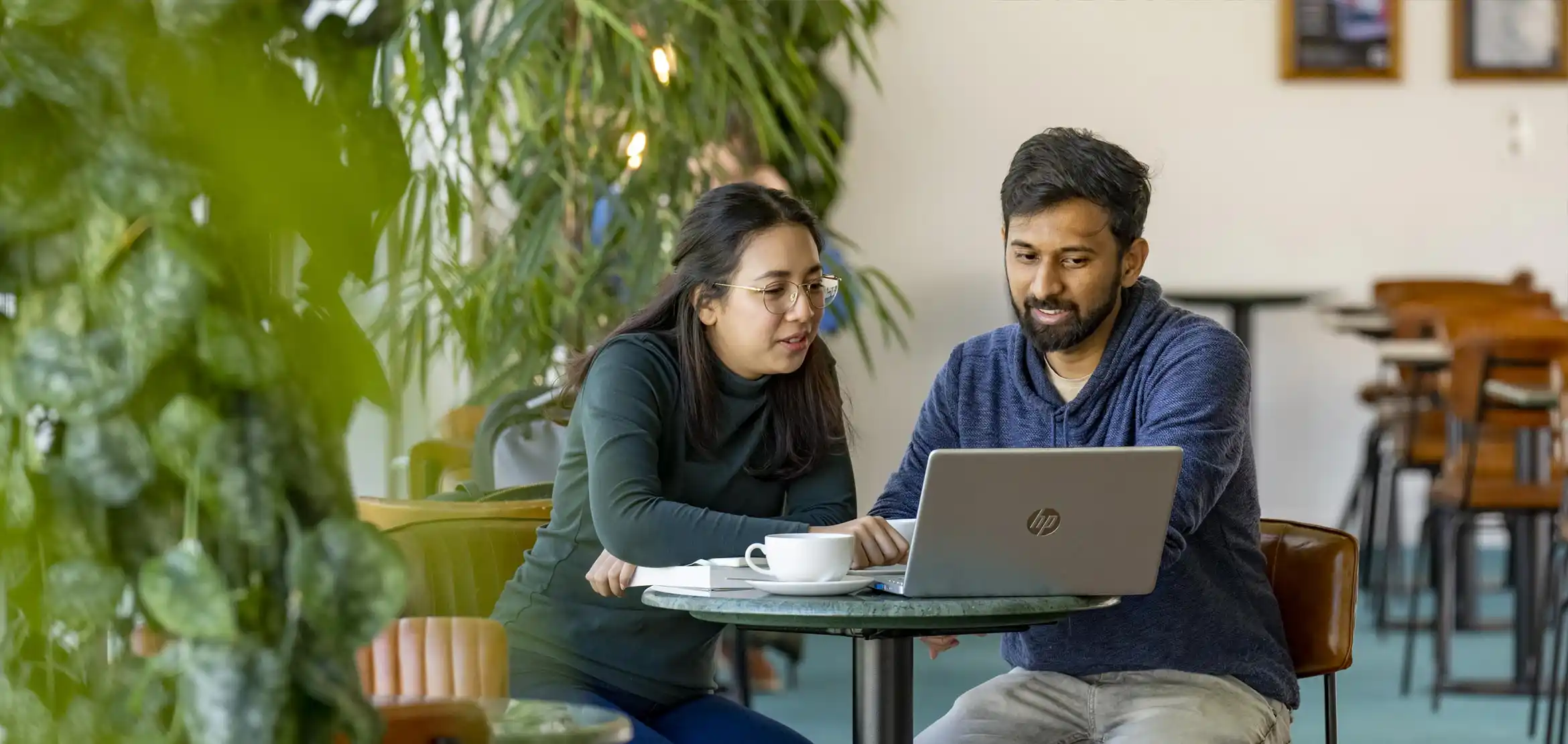 Male and female student sat at a coffee table having a conversation around a laptop.