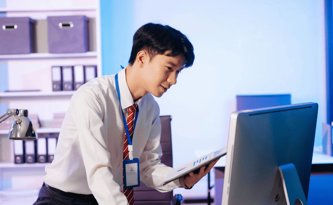 Man looks at computer screen whilst holding a clipboard