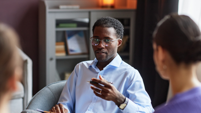 Seated man in blue shirt speaking to colleagues